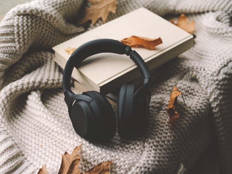 Headphones resting on a stack of books in a knitted blanket.