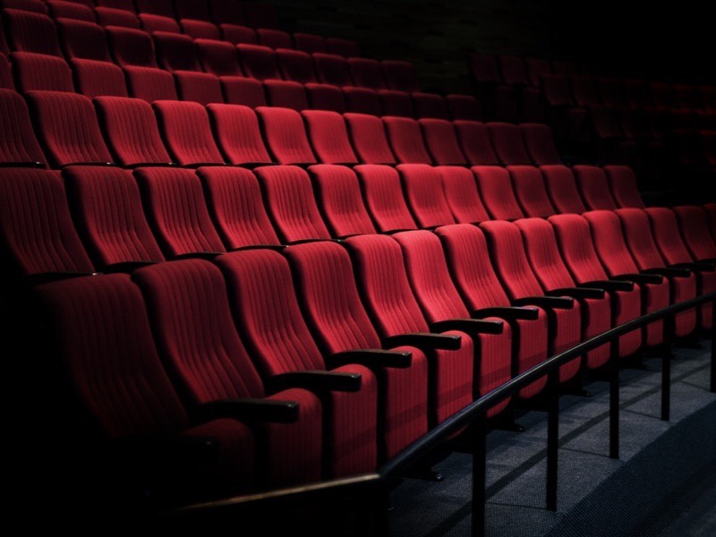 Rows of empty red seats in a darkened theatre.