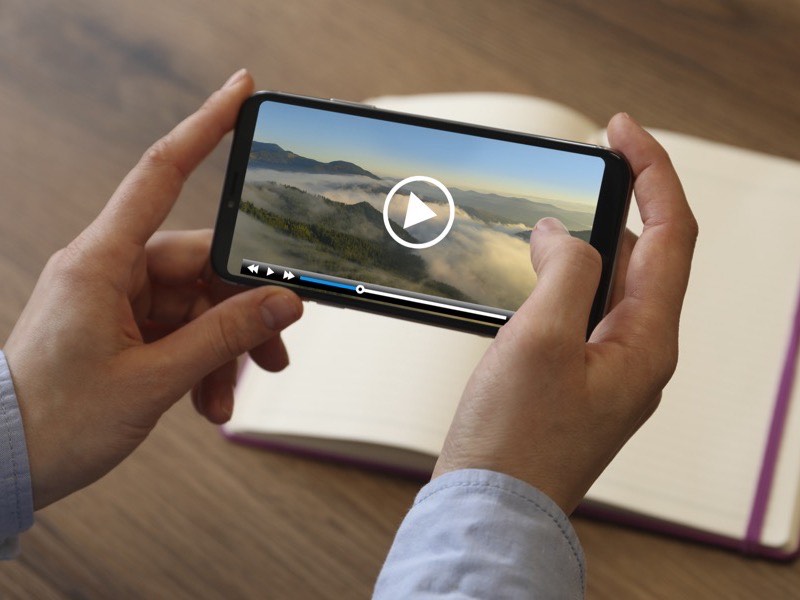 A phone held in both hands, playing a video on a wooden desk.